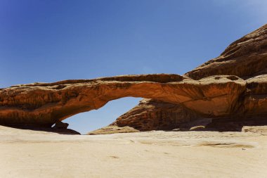 Doğal kumtaşı kemeri Wadi Rum çölünde açık mavi bir gökyüzüne karşı oyulmuş, Ürdün uzak, görkemli manzarası