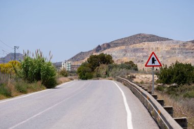 Empty rural road with intersection sign in arid mountain landscape under clear sky.