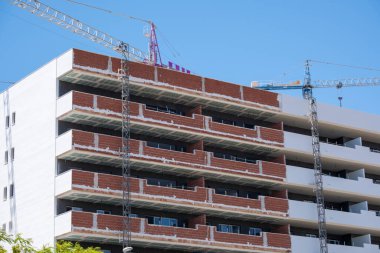 Mavi gökyüzünün altında vinçleri ve yeni binaları olan modern kentsel inşaat alanı.