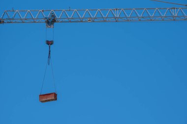 Şehir ortamında inşaat vinci mavi gökyüzüne karşı kırmızı kargo kaldırıyor.