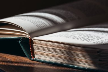 Güneş ışığı, ahşap masa üzerindeki açık kitap sayfalarını aydınlatır ve samimi bir okuma atmosferi yaratır..