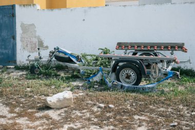 Yıpranmış duvarlara karşı yabani otlarla kaplanmış terk edilmiş bir tekne römorku..