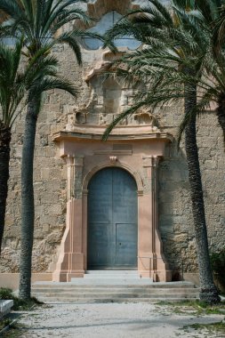 Palmiye ağaçları ve dekoratif mimarisi olan tarihi taş kilise girişi..