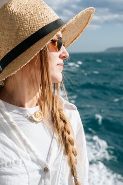 Hasır şapkalı kadın güneşli bir günde okyanus esintisinin tadını çıkarıyor..