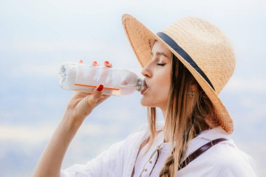 Güneş şapkalı kadın güneşli bir günde açık havada ferahlatıcı bir şeyler içiyor..