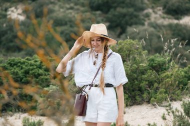 Beyaz elbiseli ve hasır şapkalı genç bir kadın doğa yürüyüşünün tadını çıkarıyor..