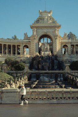 Büyük bir mimari ortamda tarihi su çeşmesinin yanında yürüyen bir kadın..