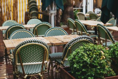 Güzel bir açık hava kafe sahnesi, dokuma sandalyeleri ve sade ahşap masaları olan rahat bir teras ortamında..