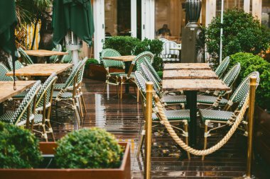 Islak ahşap güvertesi ve yağmurlu bir günde klasik bistro sandalyeleri olan rahat bir kafeterya terası..
