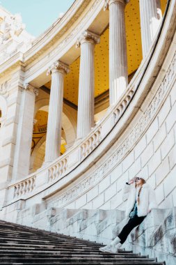 Şık şehir ortamında klasik sütunlarla mimari basamaklarda dinlenen kadın.