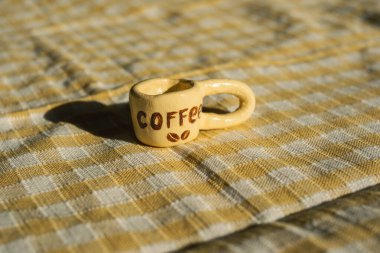 Damalı kumaş üzerine minyatür kahve fincanı: günlük tekstil ürünlerinde eğlenceli detaylar.