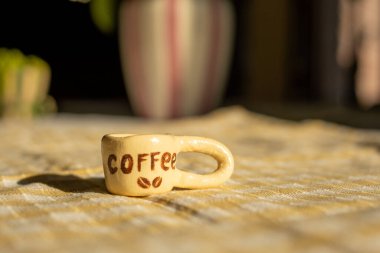 Güneşli mutfak dekorunda kareli masa örtüsünün üzerindeki küçük seramik kahve kupası..