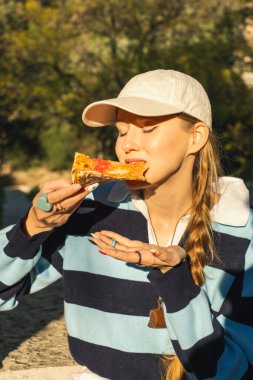 Güneşli park ortamında pizza yiyen bir kadın..