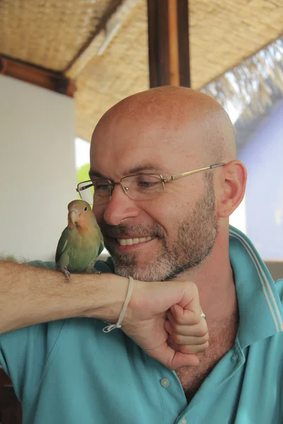 smiling bald man with a beard with a parrot on his hand