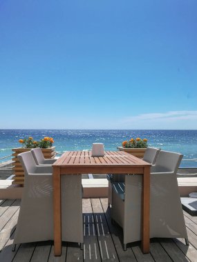 Açık havada deniz kenarına yaslanmış rattan sandalyeli yemek masası.