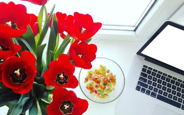 Buket tulip merah di vas dekat stand laptop pada jendela putih — Stok Foto