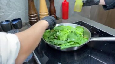 Aşçı metal bir tavada ıspanak yapraklarını kızartır ve karıştırır.