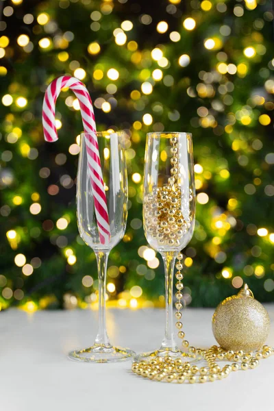 Şeker kamışı ve altın noel ağacı boncuklu şampanya bardakları bir çelengin ışıklarına karşı beyaz bir masada duruyor.