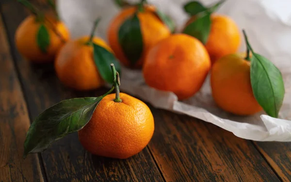 Tahta bir masanın üzerinde yaprakları olan mandalinalar.