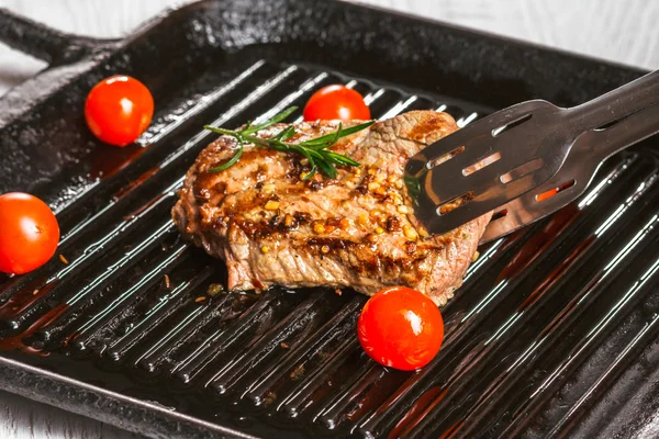 Bife segurando fórceps e tomates cereja em uma panela — Fotografia de Stock