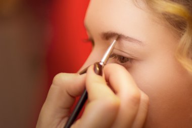 Kalıcı makyaj sanatçı uygulayarak parlak temel rengi göz farı modelinin göz ve göz farı bir kabuk arka plan üzerinde tutarak yakın çekim