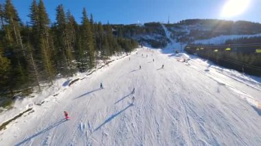 Pürüzsüz FPV insansız hava aracı açık güneşli bir günde dağlarda kış sporlarının tadını çıkaran kayakçılarla karlı yamaçlarda uçuyor. Seyahat, yaşam tarzı, tatiller ve macera temaları için mükemmel.