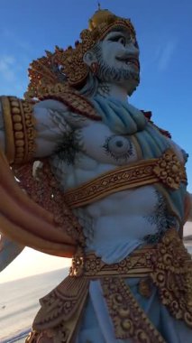 Endonezya, Bali 'de gün batımında görkemli okyanus manzaralı heykelin etrafında uçan FPV dronu. Adaların altın ışığı, dalgaları ve kültürel güzelliği..