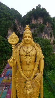 Malezya 'daki Batu Mağaraları' ndaki altın Murugan heykelinin sinematik FPV insansız hava aracı görüntüleri. Rengarenk merdivenleri, kireçtaşı uçurumları ve yemyeşil alanları seyahat ve kültürel temalar için idealdir..