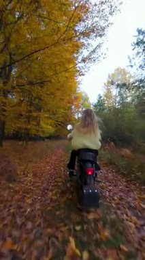 Sonbahar yapraklarıyla kaplı ormanda motosiklet süren bir kadının sinematik FPV görüntüsü. Manzaralı sonbahar manzarası, rahat macera ve sinematik yaşam tarzı..