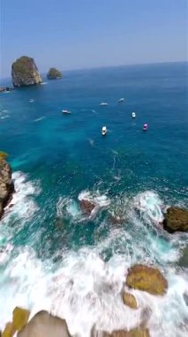 Manta Point, Nusa Penida, Bali, Endonezya 'daki turkuaz suların üzerinde FPV insansız hava aracı uçuşu. Tekneler, kayalıklar ve canlı mavi deniz. Seyahat, doğa ve okyanus projeleri için mükemmel..