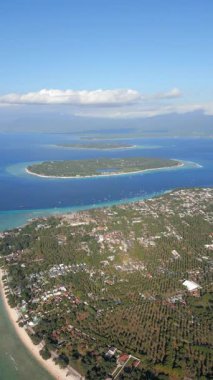 Endonezya 'daki Gili Trawangan adasının arka planda Gili Meno ve Gili Air ile hava görüntüsü. Turkuaz su ve mercan resifleriyle tropik deniz manzarası.