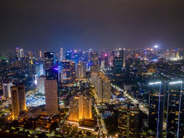 Aydınlatılmış Jakarta kentinin insansız hava aracı görüntüsü ve gece iş bölgesinde yoğun trafik Endonezya modern kentsel manzarasını vurguluyor