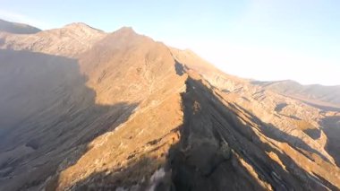 Endonezya 'nın doğu Java kentindeki engebeli Bromo volkanik uçurumları ve kayalık tepelerden FPV insansız hava aracı uçuşu. Dinamik hareket dramatik manzarayı vurgular, macera ve doğa temaları için mükemmeldir..