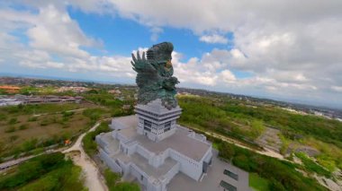 Endonezya, Bali 'deki Garuda Wisnu Kencana heykelinin sinematik FPV insansız hava aracı görüntüleri. Arka planda şehir manzarası ve okyanus olan anıtsal kültür simgesi, Bali mirası ve Hindu mitolojisinin sembolü.