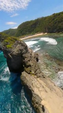 Dramatik uçurumlar boyunca FPV insansız hava aracı uçuşu ve Endonezya 'nın Nusa Penida Adası' ndaki Atuh Sahili 'nde kristal berrak turkuaz okyanus. Tropik sahil şeridi, güçlü dalgalar ve egzotik seyahat manzarası..