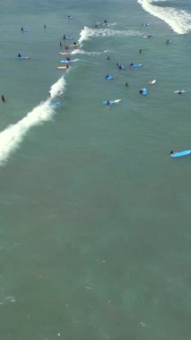 Acemi sörfçülerin Endonezya, Bali 'de kıyıya yakın dalgalarda kürek çekip sörf derslerini gösteren hava aracı görüntüsü. Popüler sörf merkezi, okyanus aktivitesi ve tropikal plaj yaşam tarzı..