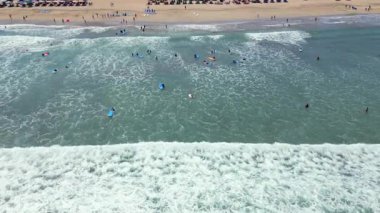 Acemi sörfçülerin beklediği, kürek çektiği ve Endonezya, Bali 'de kıyıya yakın küçük dalgalarda sörf derslerinin yukarıdan aşağıya insansız hava aracı görüntüsü. Popüler plaj aktivitesi ve tropikal sörf yaşam tarzı.