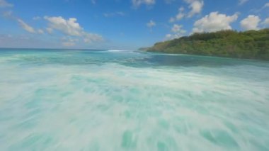 FPV insansız hava aracı kristal berrak turkuaz su üzerinde uçuyor ve Endonezya, Bali yakınlarında okyanus dalgaları sıçrıyor. Tropik deniz manzarası, yaz yolculuğu, özgürlük, macera ve okyanus enerjisi.