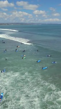 Acemi sörfçülerin Endonezya, Bali 'de kıyıya yakın dalgalarda kürek çekip sörf derslerini gösteren hava aracı görüntüsü. Popüler sörf merkezi, okyanus aktivitesi ve tropikal plaj yaşam tarzı..