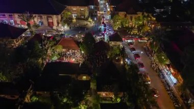 Ubud, Bali 'nin merkezinde yoğun sokak trafiği, aydınlık binalar ve tropikal bahçeler ve canlı gece ışıkları ile çevrili Ubud Sarayı' nın yakınında görünür bir açık hava sahnesi var..