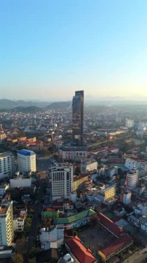 Vietnam 'ın ortasındaki Hue City siluetinin insansız hava aracı görüntüsü. Altın saatinde arka planda dağlarla birlikte yerleşim yerlerinin tepesinden yükselen modern gökdelenler..