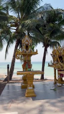 Tayland 'da tropik plajlarda sunulan geleneksel Tayland ruh evleri. Ada kıyı şeridindeki turkuaz deniz kıyısındaki palmiye ağaçlarının altındaki kültürel türbe.