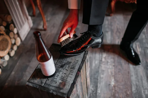 Schoonmaken van schoenen op houten achtergrond. zwarte schoen met een borstel. Rode verstelbare sleutel. Trouwringen. bierfles. Houten doos en brandhout — Stockfoto