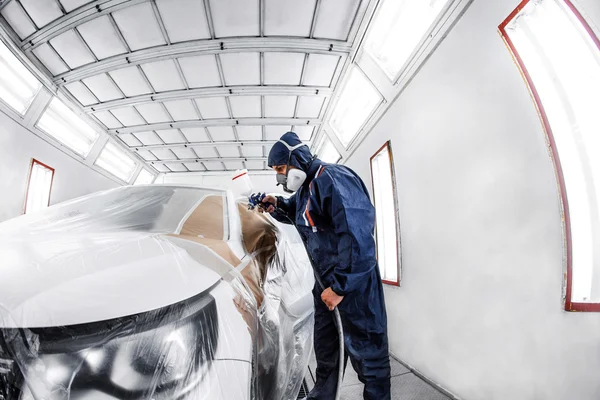 Trabajador pintando un coche blanco en un garaje especial, con traje y equipo de protección —  Fotos de Stock