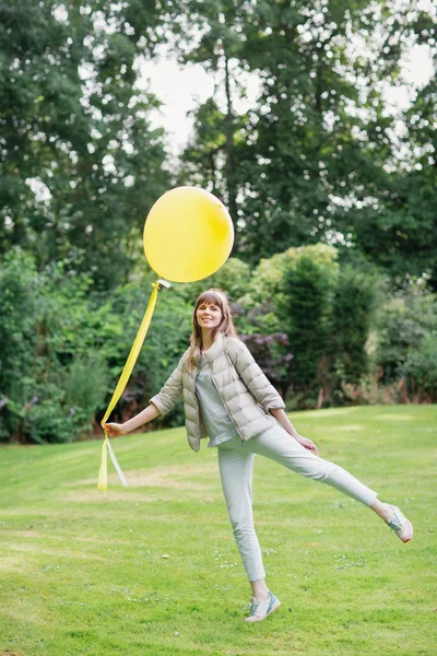 Con un palloncino giallo. Felice bella giovane ragazza studio a piedi nel giardino europeo. Sta guardando la telecamera. — Foto Stock