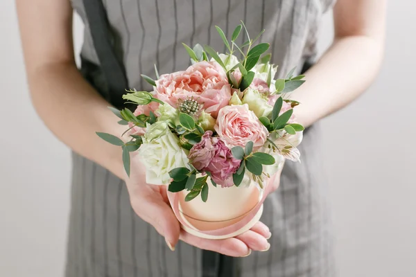 Work florist, bouquet in a round box. smelling flowers holding peach roses in hat against the plastered wall.