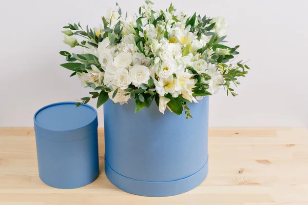 Work florist, bouquet in a round Serenity box. smelling flowers holding white roses in hat against the plastered wall.