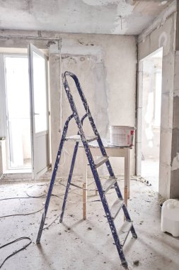 İnşaat alanındaki bir odada alüminyum merdiven işe yarıyor. Boş bir odada tamir işlemi. Tasarım için içi boş, gri beton duvar.