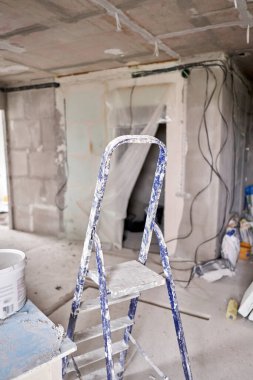 İnşaat alanındaki bir odada alüminyum merdiven işe yarıyor. Boş bir odada tamir işlemi. Tasarım için içi boş, gri beton duvar.