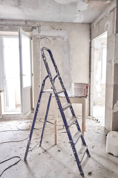 Escalera de aluminio en una habitación en construcción. Proceso de reparación en una habitación luminosa vacía. Interior vacío para el diseño, pared de hormigón gris. — Foto de Stock